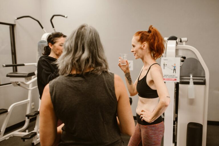 Three women chatting and hydrating in a gym environment, focusing on wellness and fitness.